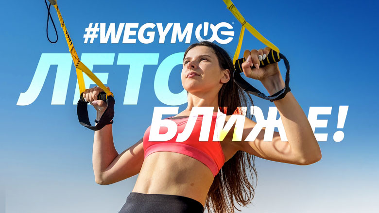 Девушка в спортивном топике занимается на петлях trx на фоне надписи #wegym Лето ближе!