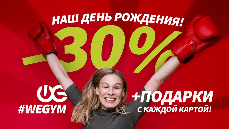 Девушка улыбается в боксерских перчатках на красном фоне с надписью WeGym Наш день рождения -30% + подарки